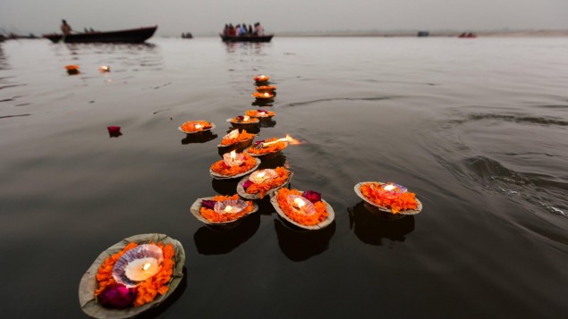 Mehrere auf Blättern orangenen Blüten gesetzte Kerzen schwimmen auf dem Wasser.